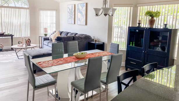 Ein modernes Wohnzimmer mit einem Glastisch, grau gepolsterten Sesseln, einem dunkelblauen Schrank und einem grauen Sofa.