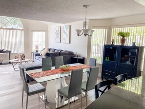 Uma sala de estar moderna com uma mesa de jantar de vidro, cadeiras estofadas cinza, um armário azul escuro e um sofá cinza.