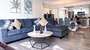 Ein modernes Wohnzimmer mit einem grauen Sofa, einem runden Couchtisch und zwei Bildern an der Wand.