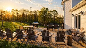 Une terrasse extérieure avec des fauteuils Adirondack, un barbecue et une vue sur une zone boisée.