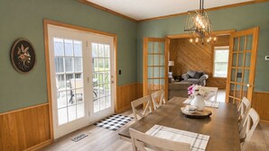 Un coin repas avec une table en bois, des chaises, un lustre et une vue à travers une porte vitrée.