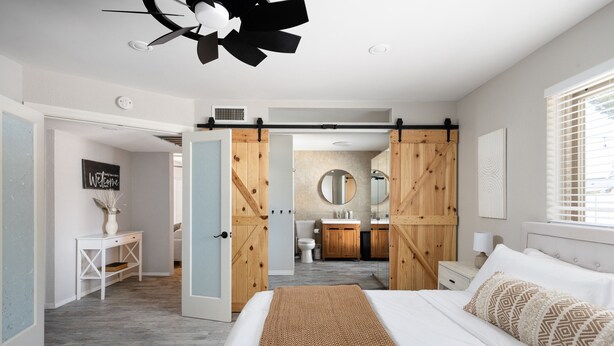 A modern bedroom with a large bed, a wooden wardrobe, a bathroom with a round mirror, and a white console table.
