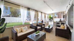 A sunlit patio with wicker furniture, a glass coffee table, and a view of a swimming pool.