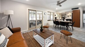 A modern living room with a brown leather sofa, a wooden coffee table, and a dining area with a white table and black chairs.