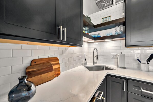 A modern kitchen with white subway tiles, dark cabinets, and a wooden cutting board. - Suite Magnolia (Waco)