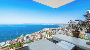 Ein Balkon mit Blick auf die Stadt und das Meer, mit einem Blumentopf und einem weißen Tisch.