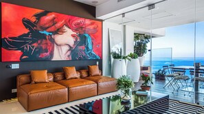 A modern living room with a large abstract painting, a leather sofa, and a view of the ocean.