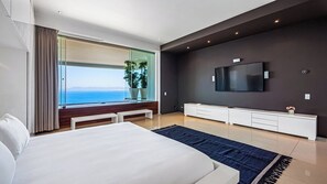 Una camera d'albergo moderna con un grande letto, una TV a schermo piatto montata a parete, un'ampia finestra vista mare e un elegante tavolino consolle bianco.