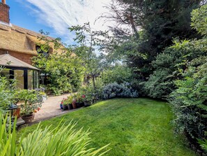 A well-maintained garden with a variety of plants and a clear pathway leading to a conservatory.