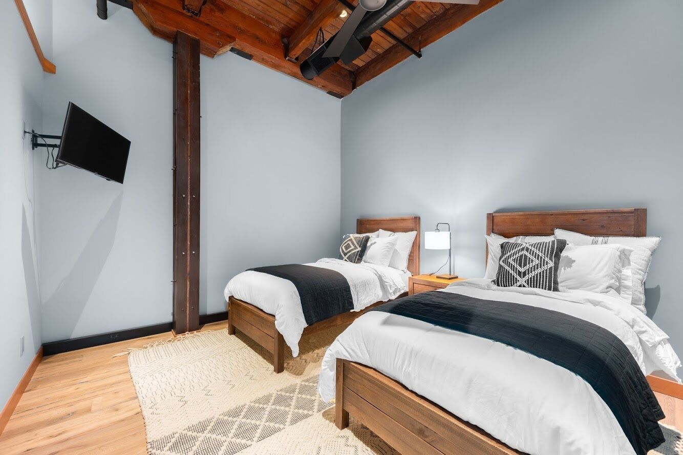Une chambre avec deux lits en bois, un téléviseur fixé au mur et un plafond en bois.