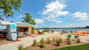 Un magasin de location de kayaks et de vélos situé au bord d’un lac, avec des kayaks et des radeaux sur le sable.