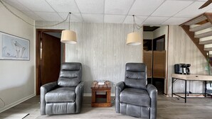 A modern living room with two leather armchairs, a wooden coffee table, and a staircase in the background.
