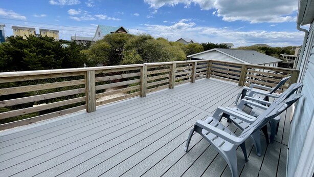 A wooden deck with lounge chairs, overlooking a residential area with houses and trees.
