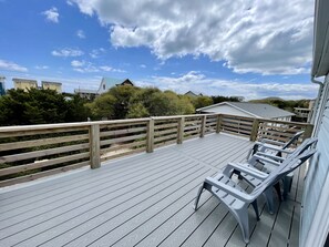 Una terraza de madera con sillones de descanso, con vista a una zona residencial con casas y árboles.