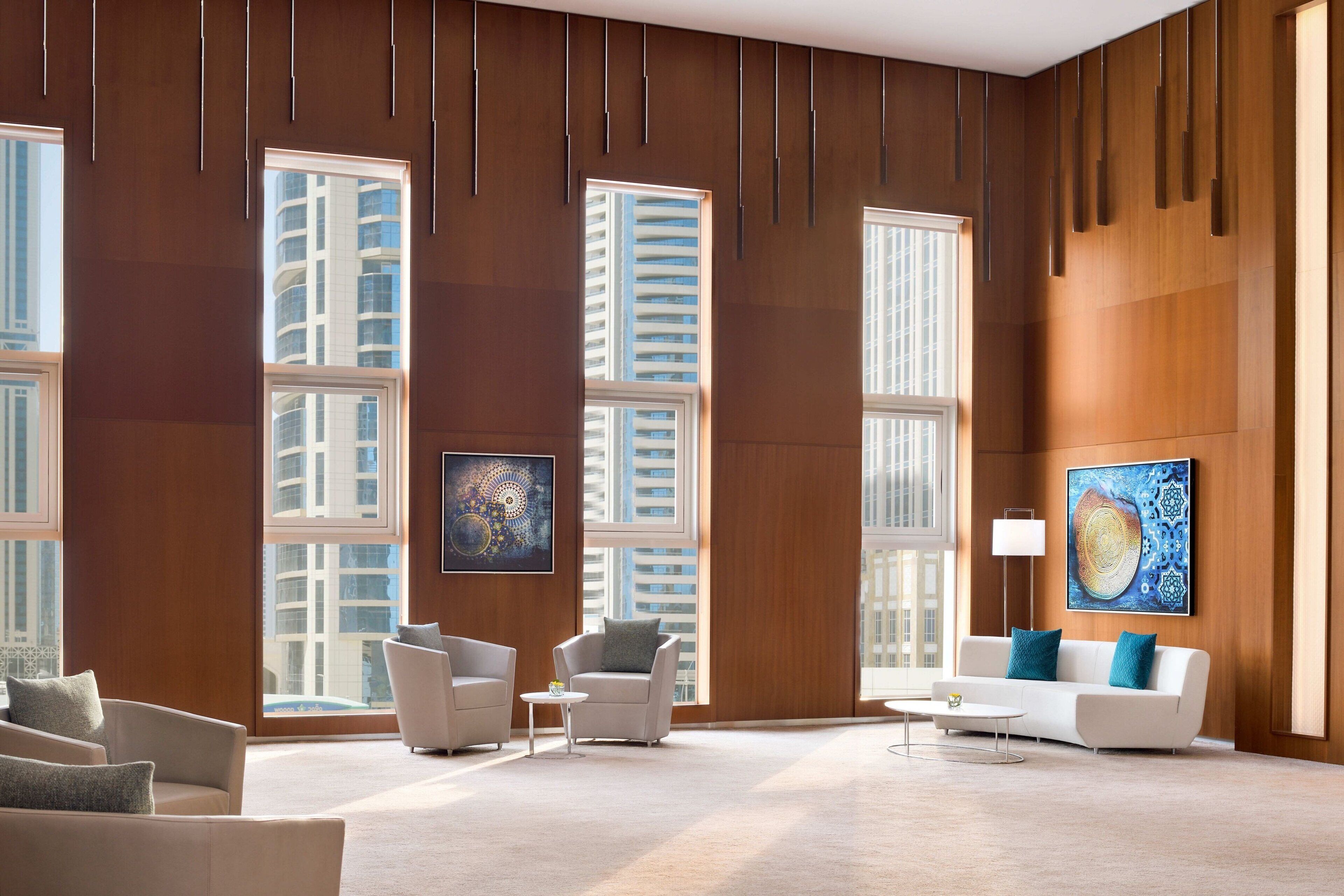 A modern hotel lobby with large windows, a white sofa, and two armchairs.