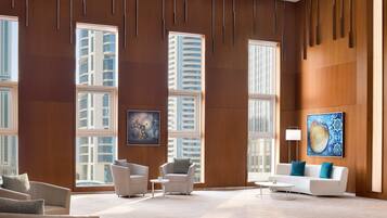 A modern hotel lobby with large windows, a white sofa, and two armchairs.