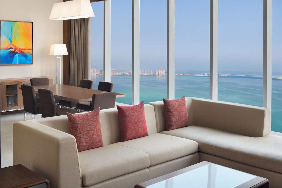 A modern hotel room with a large window offering a view of the sea and cityscape.