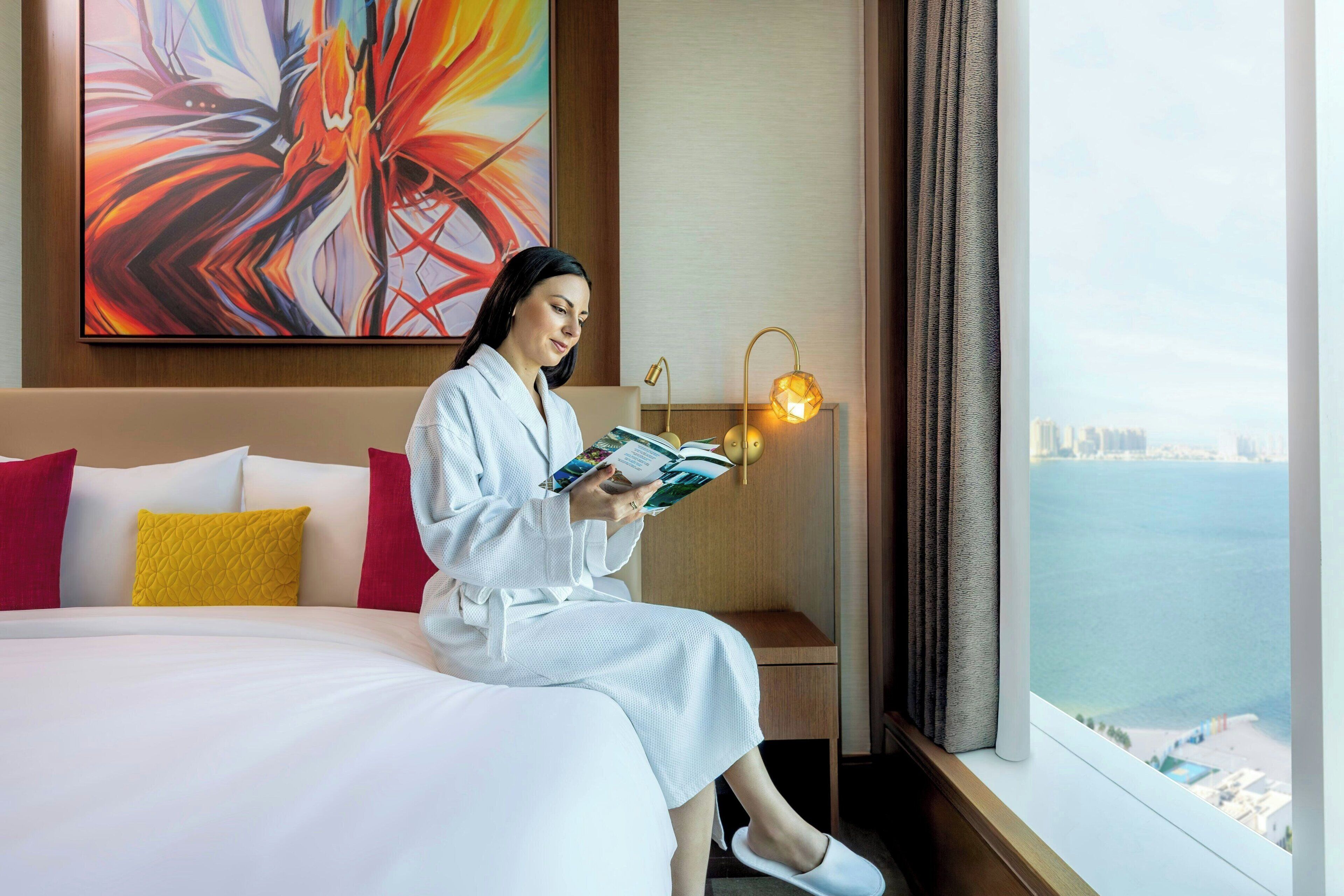 A hotel room with a large bed, a bedside table with a lamp, and a view of the sea.
