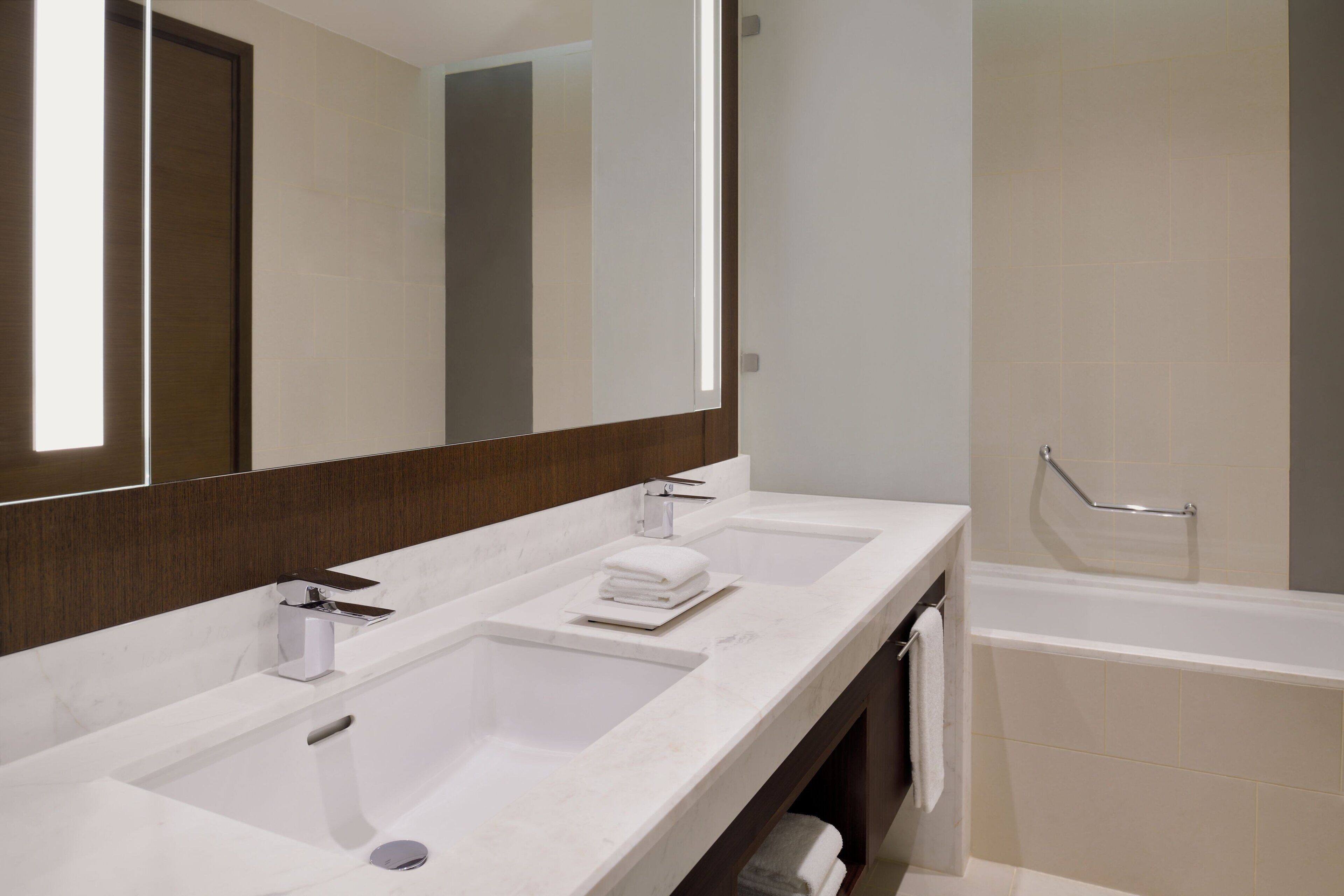 A modern bathroom with two sinks, a large mirror, and a bathtub.