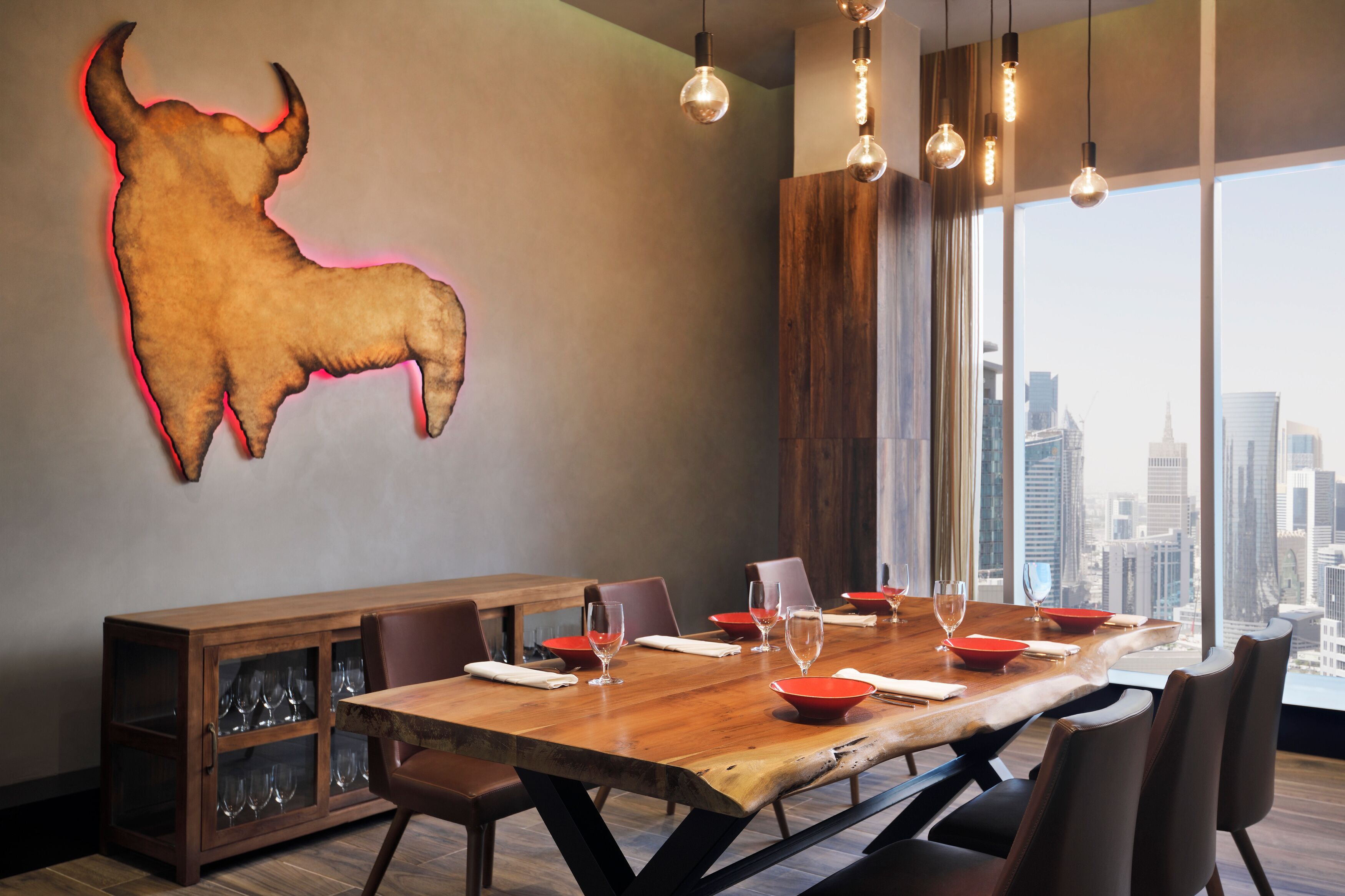 Un espace repas moderne avec une grande table en bois, des bols rouges et des verres à vin.