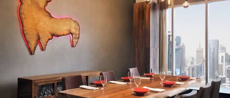 Un espace repas moderne avec une grande table en bois, des bols rouges et des verres à vin.