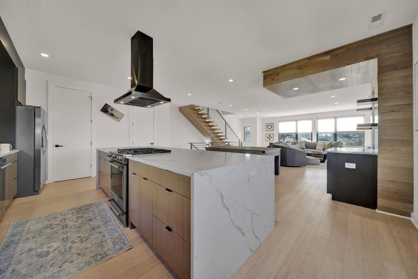 A modern kitchen with a central island, built-in oven, and a stainless steel range hood.