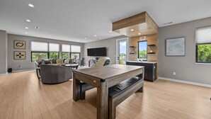 Un salón espacioso con una mesa de comedor de madera, un sofá gris y un amplio ventanal con vistas a zonas verdes.