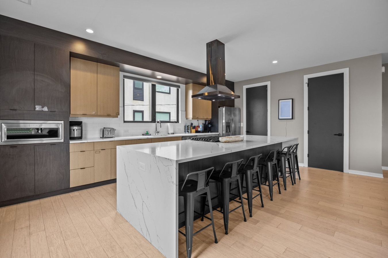 A modern kitchen with a large island, dark wood cabinets, and a stainless steel range hood.