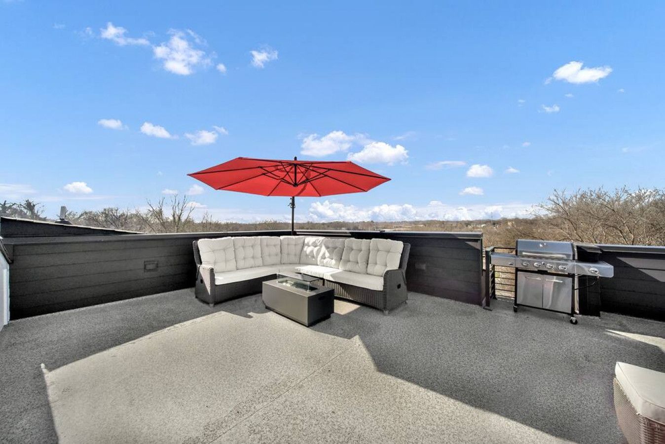 A rooftop patio with a sectional sofa, a red umbrella, and a grill.