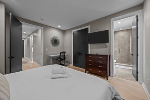 A bedroom with a large bed, a desk, a dresser, and a shower area.