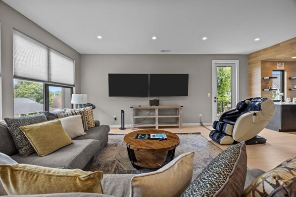 A modern living room with a sofa, coffee table, massage chair, and a flat-screen TV.