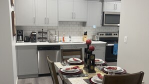 A modern kitchen with white cabinets, a microwave, and a dishwasher. There is a dining table set with plates, glasses, and cutlery.