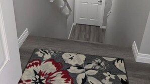 A staircase with a white door at the top, a patterned rug at the bottom, and a white wall on the left.