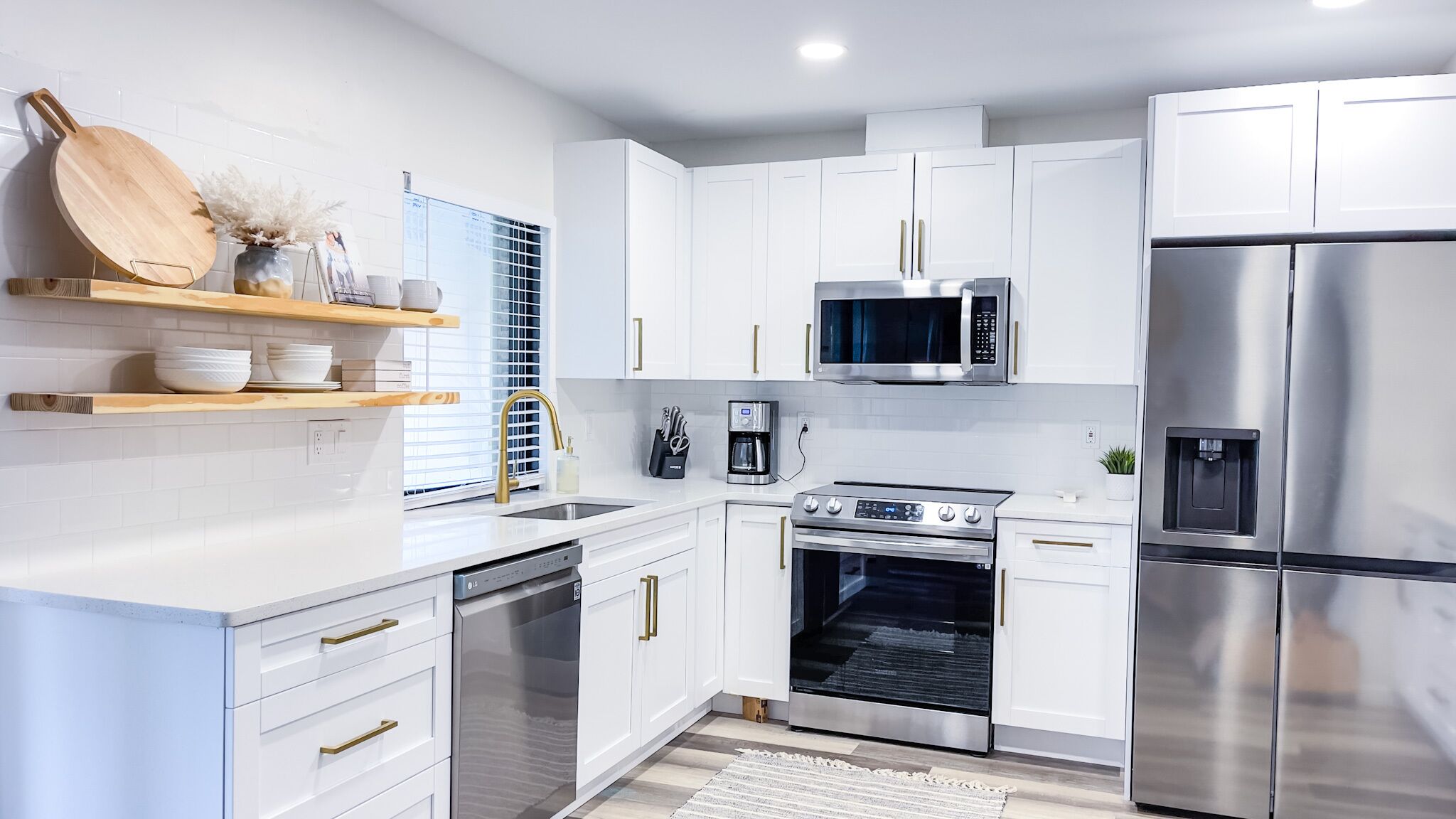 A modern kitchen with white cabinets, stainless steel appliances, and wooden shelves.