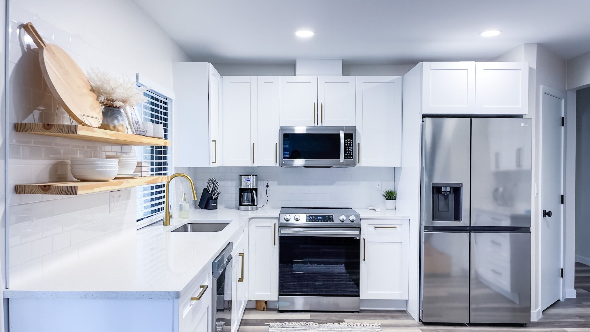 Una cocina moderna con armarios blancos, un refrigerador de acero inoxidable, un horno y un microondas.