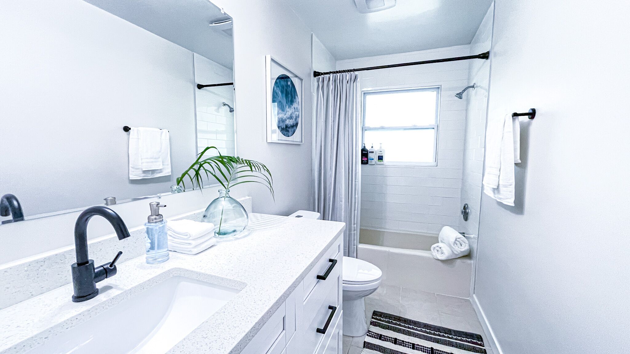 A modern bathroom with a large mirror, a sink with a faucet, a toilet, and a shower area.