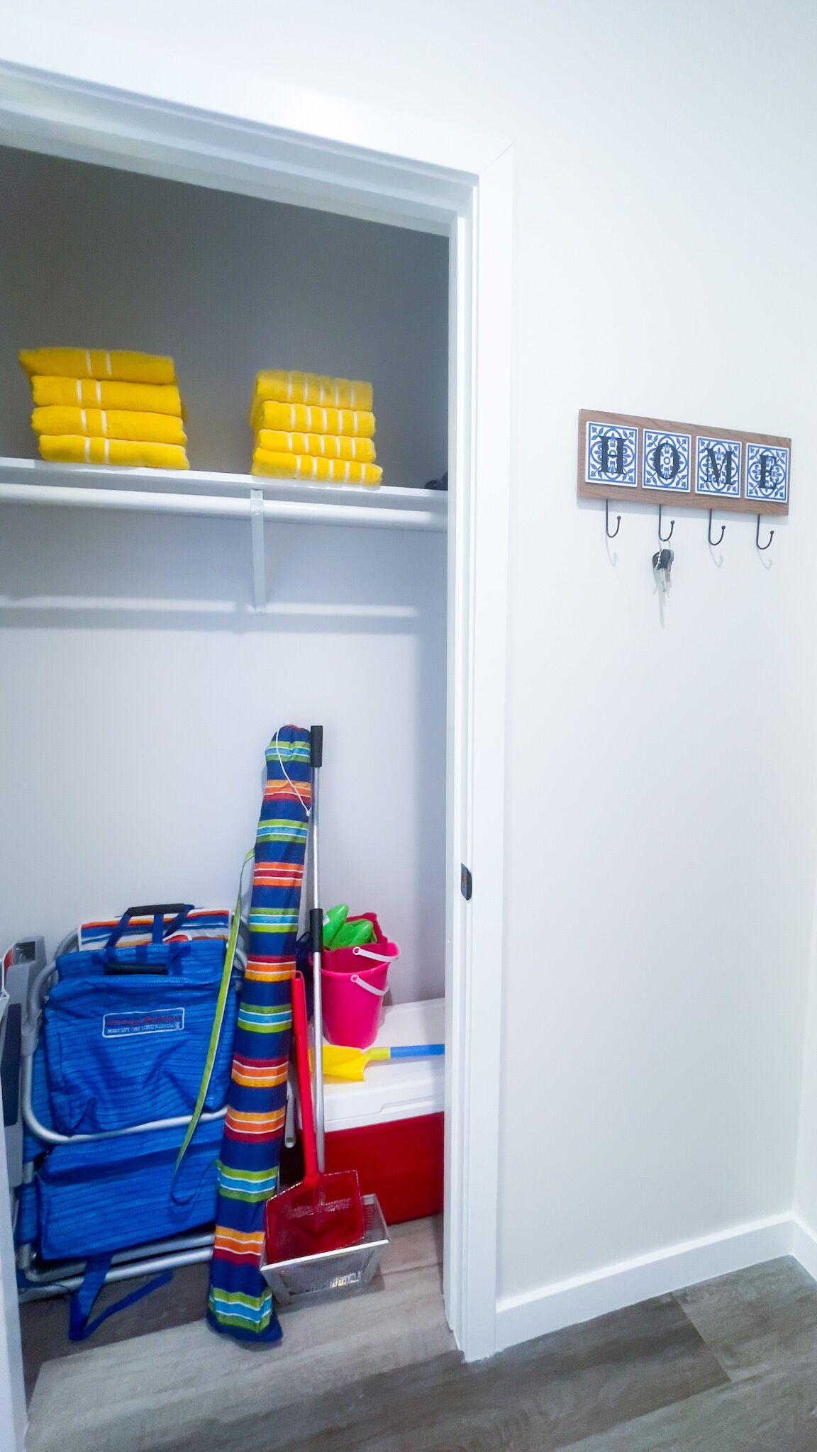 A storage closet with shelves holding yellow towels, a blue striped bag, and cleaning supplies.