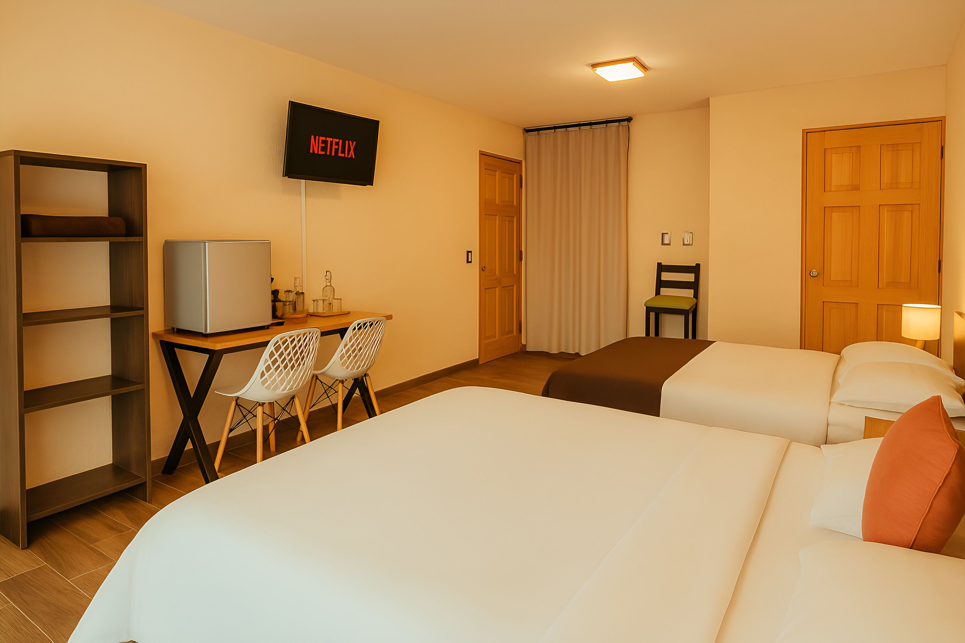 Habitació d'hotel amb dos llits, un escriptori amb televisió, una prestatgeria i una cadira.