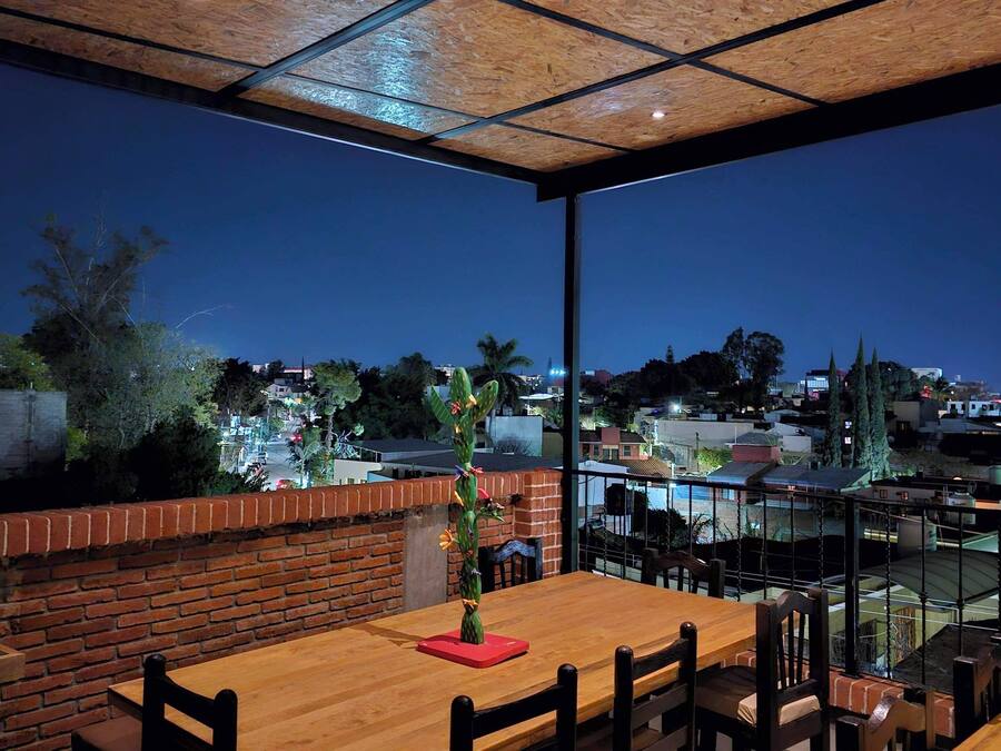 A dining area with a wooden table and chairs, a cactus decoration, and a view of a residential area at night.