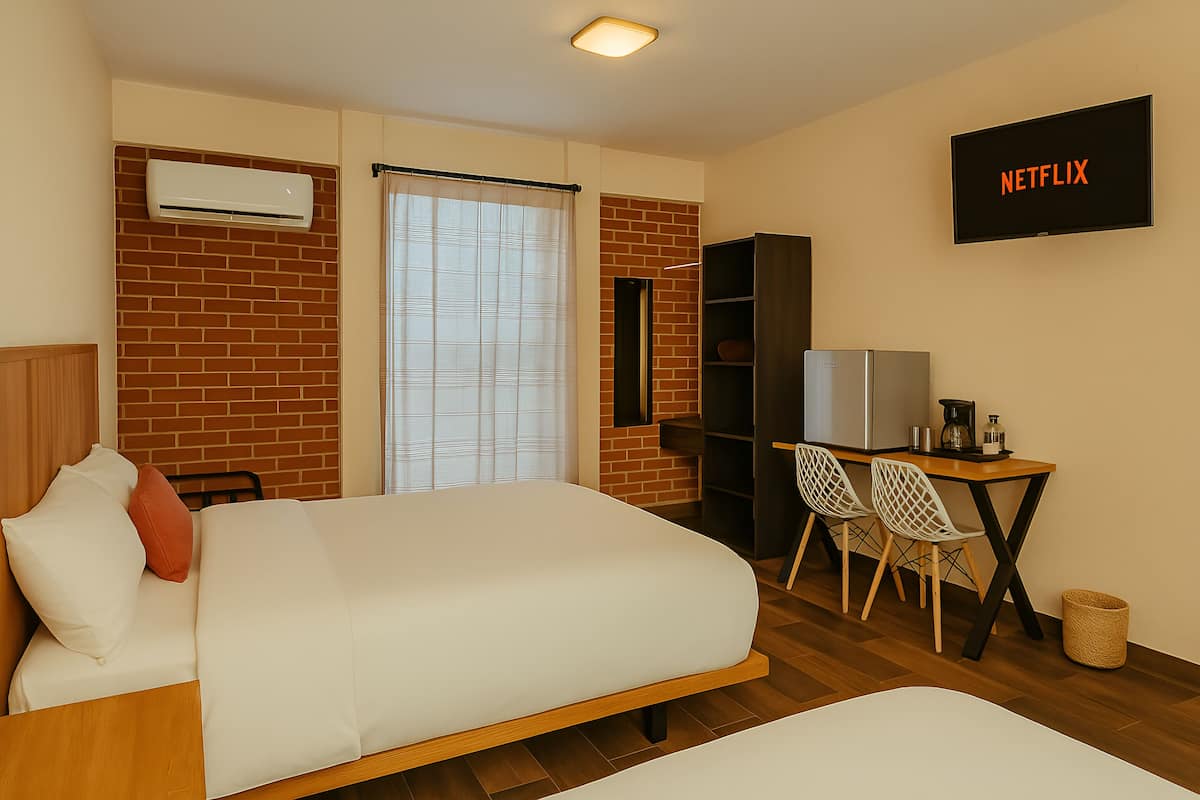 A hotel room with a bed, a desk with chairs, a TV, and a bookshelf.