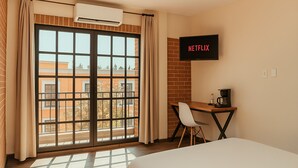 A hotel room with a large window, a desk with a chair, a bed, and a wall-mounted TV displaying "NETFLIX". - Casa Acueducto (Oaxaca)