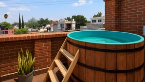 A wooden hot tub on a rooftop terrace with a brick wall and a potted plant. - Casa Acueducto (Oaxaca)