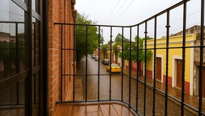 A balcony with a wooden floor and metal railing overlooking a street with cars and buildings. - Casa Acueducto (Oaxaca)