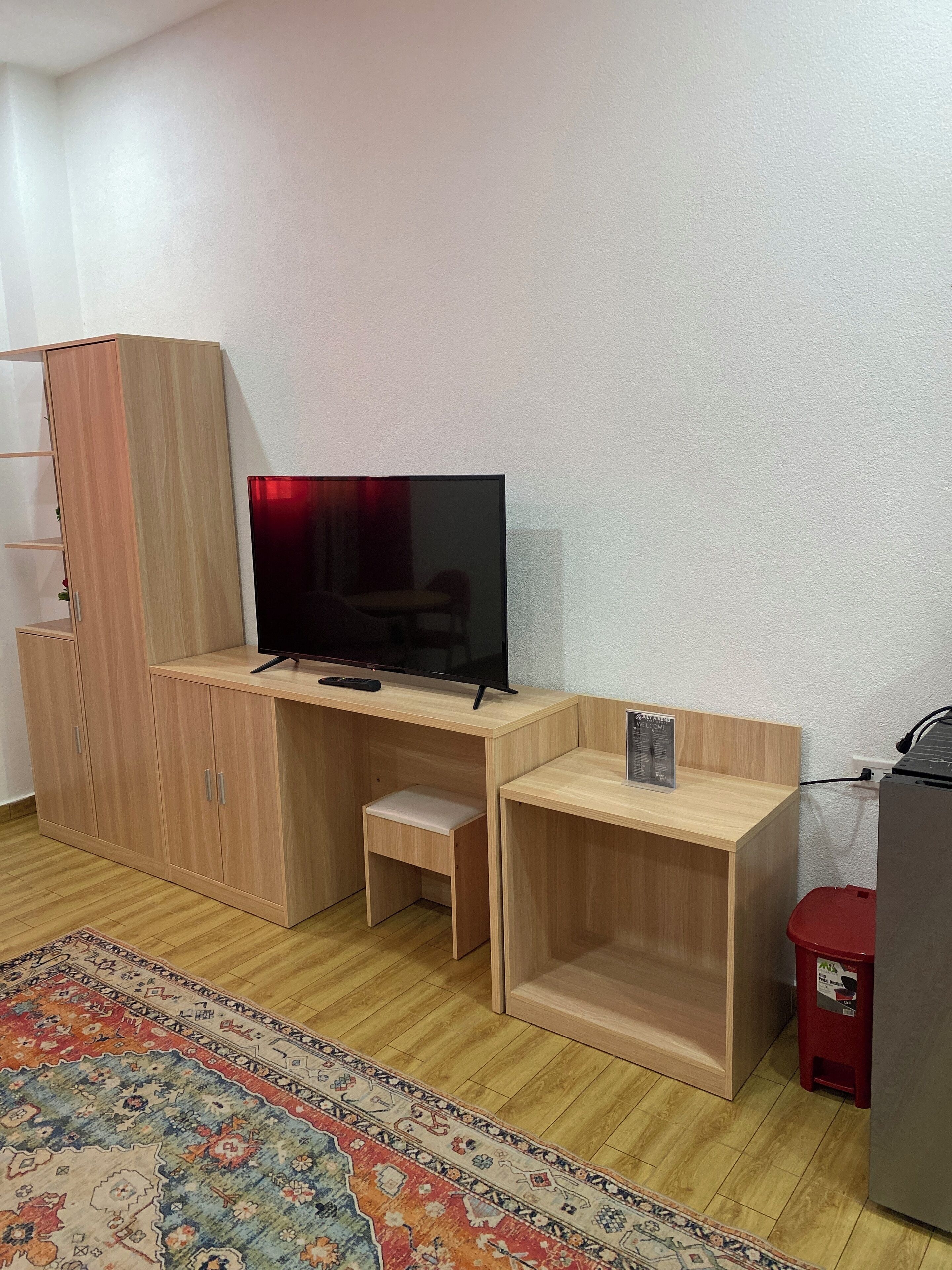 A compact living space with a wooden desk, a television, and a small stool.