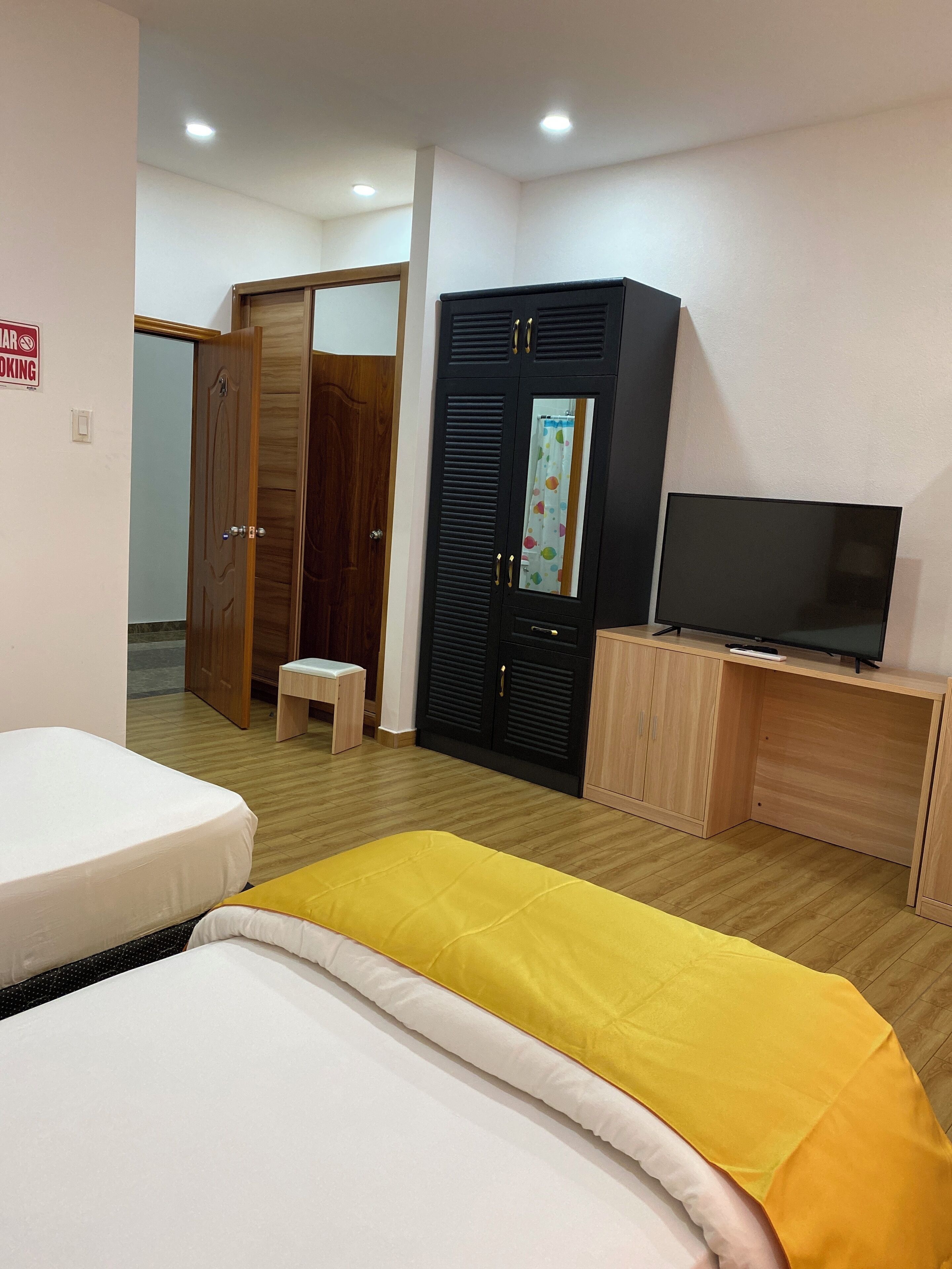Habitación de hotel con cama, televisión sobre un soporte de madera, armario y un taburete pequeño.