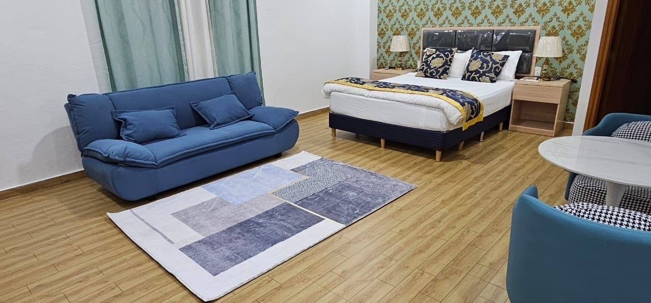 A room with a blue sofa, a bed with a patterned bedspread, a small table, and a patterned rug.