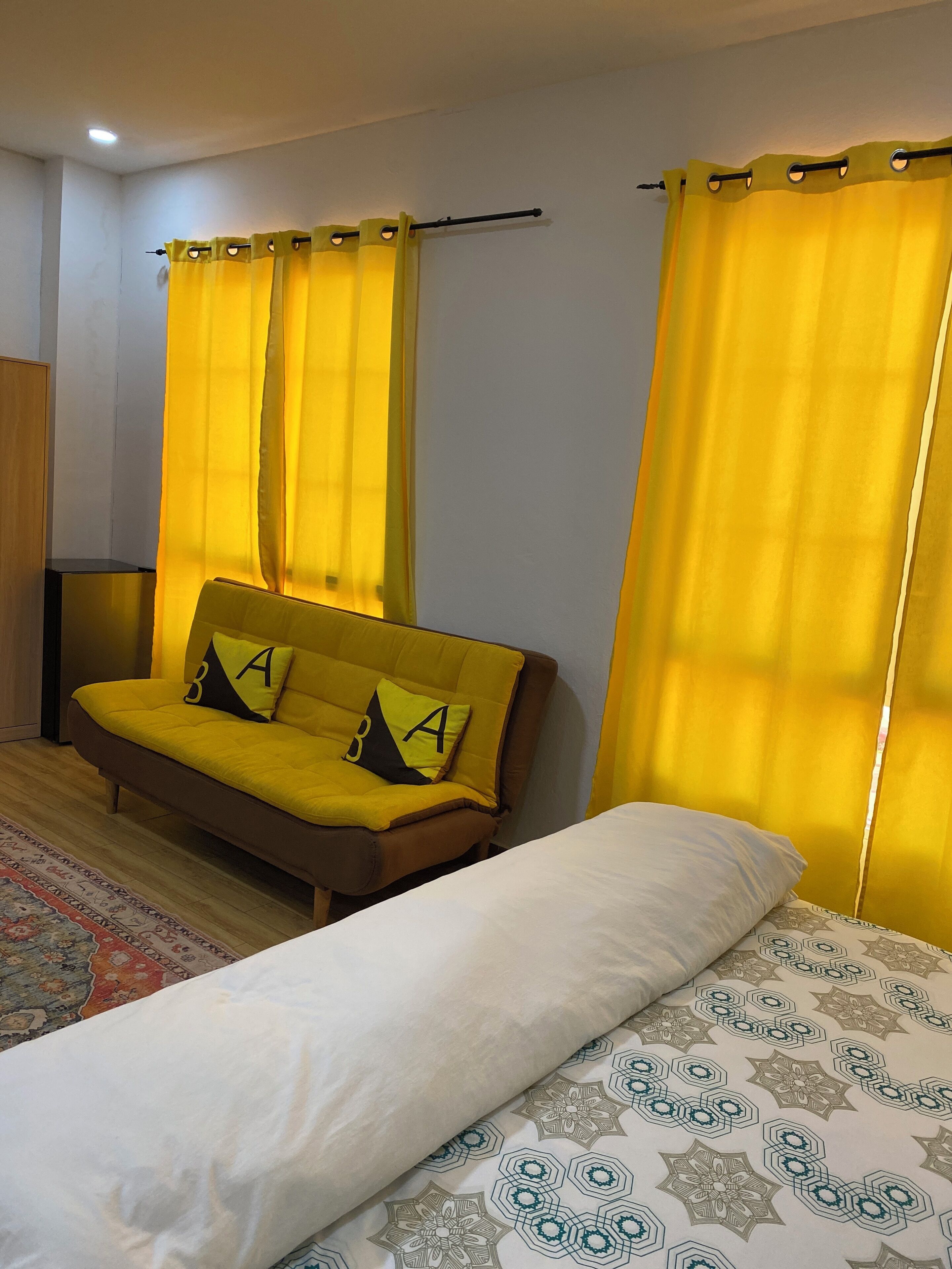 A bedroom with a bed, a sofa, and yellow curtains.