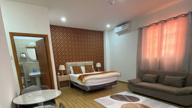 A hotel room with a bed, a sofa, a small round table, and a chair. There is a bathroom visible through an open door. - July Apartments (Philipsburg)