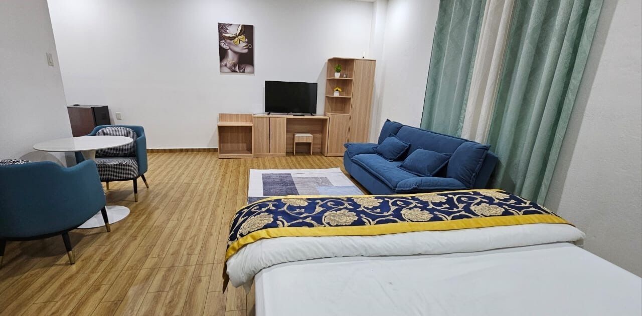 Una camera d'albergo con un letto, un divano blu, una scrivania e una televisione, e una poltrona.