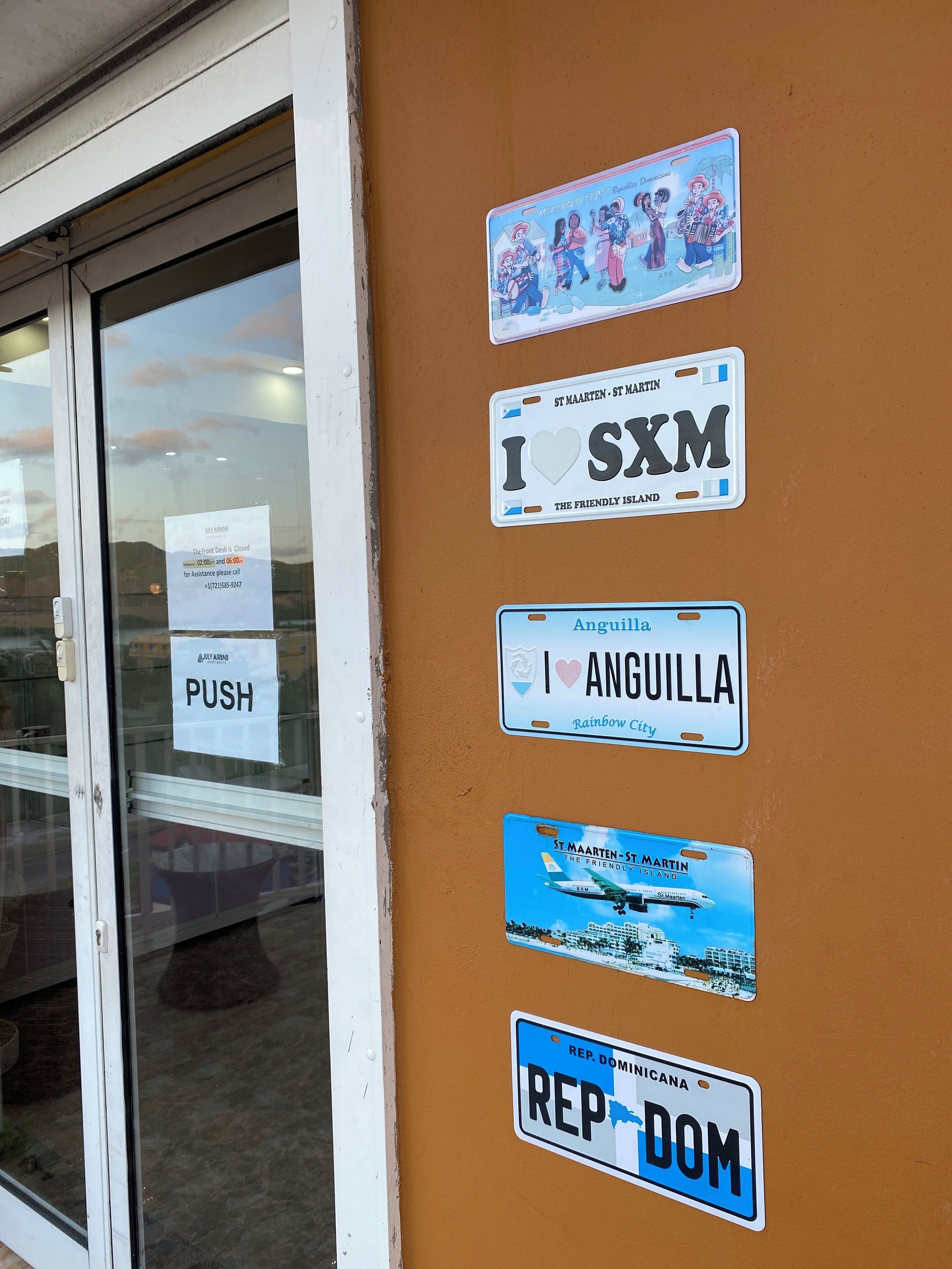 Een muur met diverse stickers, waaronder een 'DUW'-bordje, een sticker van Anguilla en een sticker van Sint Maarten - Sint Martin.